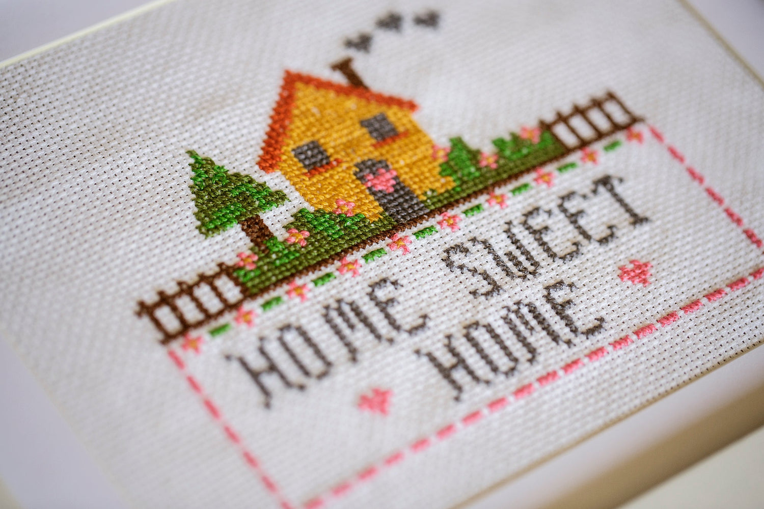 Tela bordada en punto de cruz con diseño de una casita y texto home sweet home.