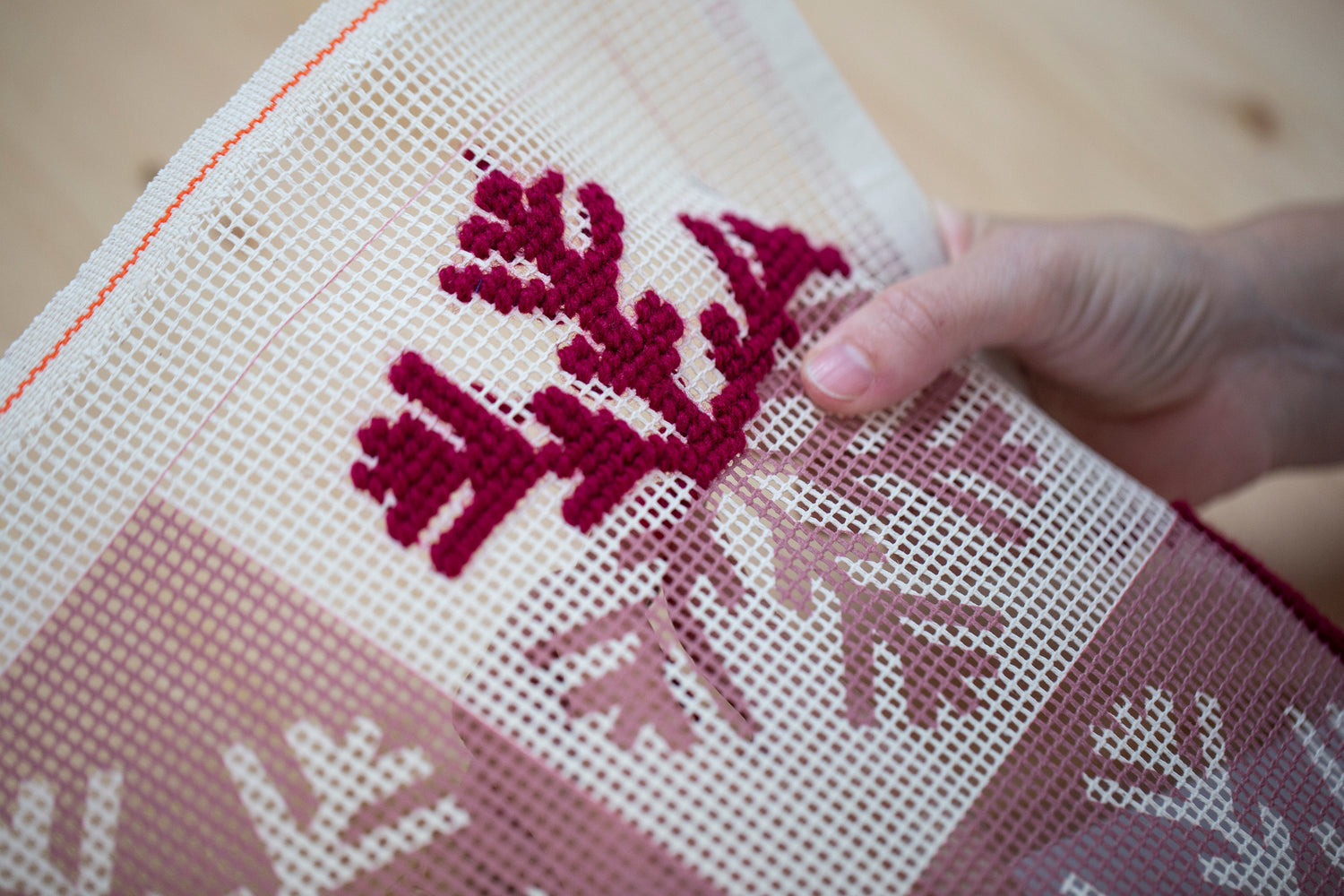 Una mano bordando a mano un cañamazo con un motivo navideño. 