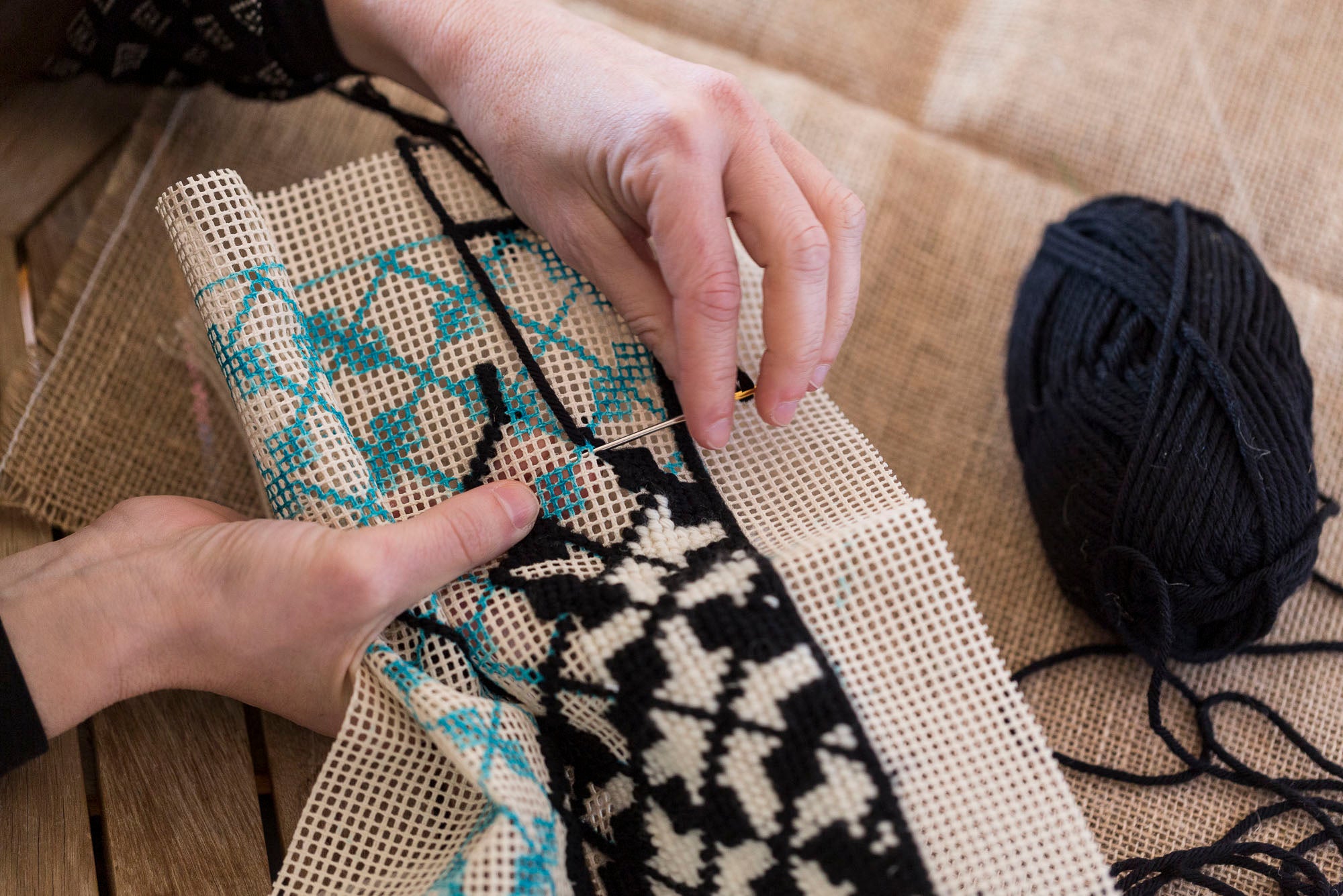 manos bordando sobre un cañamazo con la técnica del petit point o punto de cruz con lana gruesa.